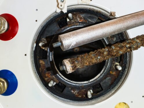 Two water heater anode rods are shown above an open heater tank—one new and clean, the other old and heavily corroded. Visible red and blue pipe connections highlight the importance of regular Water Heater Maintenance and Anode Rod Replacement. | High 5 Plumbing, Heating & Cooling