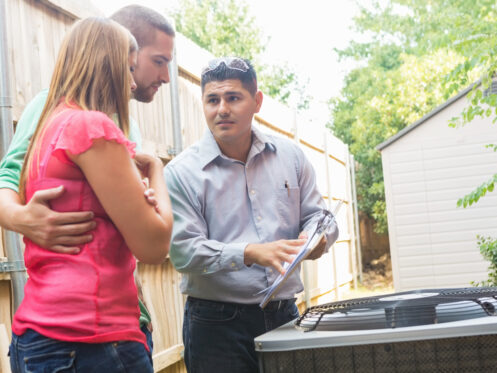 A man in a button-up shirt holds a clipboard and explains heating and cooling tips to a couple standing outside next to an outdoor AC unit near a wooden fence and shed. | High 5 Plumbing, Heating & Cooling