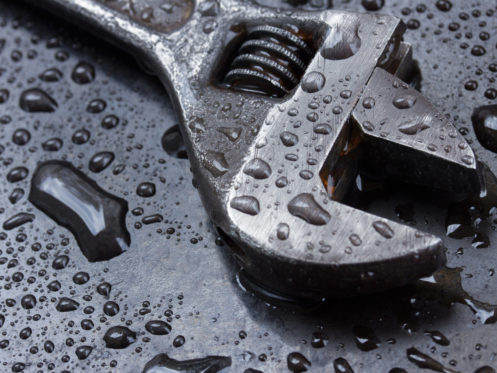 A close-up of a metal adjustable wrench lying on a wet, dark surface, covered in water droplets. | High 5 Plumbing, Heating & Cooling