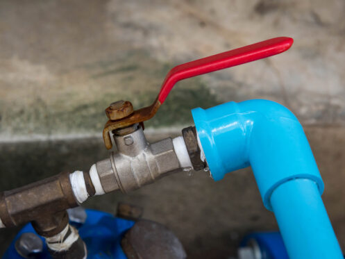 Close-up of a metal water shut-off valve with a red lever handle connected to a blue PVC pipe at a right angle, with a small water leak visible at the joint—an essential detail for any shut-off valve guide. | High 5 Plumbing, Heating & Cooling