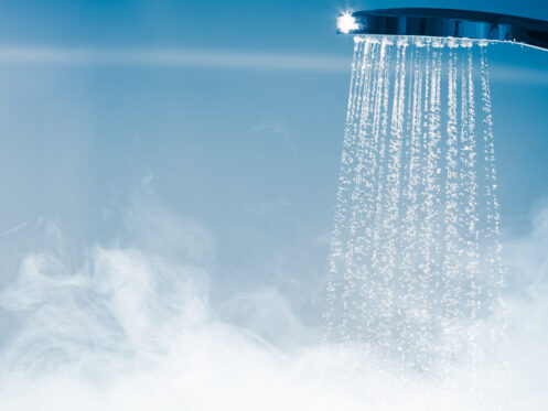 A close-up of a showerhead spraying water, with visible steam rising below, indicating hot water in use. The soft blue background adds to the clean, fresh atmosphere—perfect inspiration for luxurious bathroom or shower upgrades. | High 5 Plumbing, Heating & Cooling