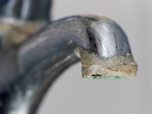 A close-up of a metal faucet with a significant buildup of white and brown limescale deposits around the spout highlights the importance of limescale prevention in the home. | High 5 Plumbing, Heating & Cooling