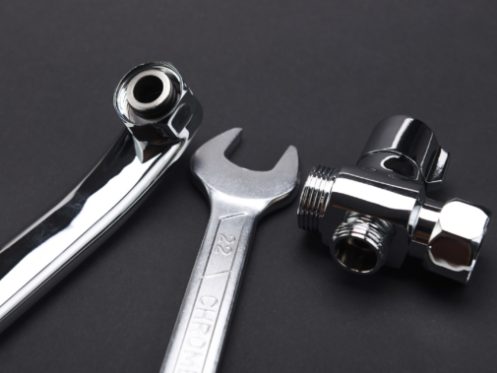 A close-up of a chrome-plated wrench and two metal plumbing fittings on a plain black background, highlighting essential tools used to fix frozen pipes and prevent frozen pipes during winter. | High 5 Plumbing, Heating & Cooling